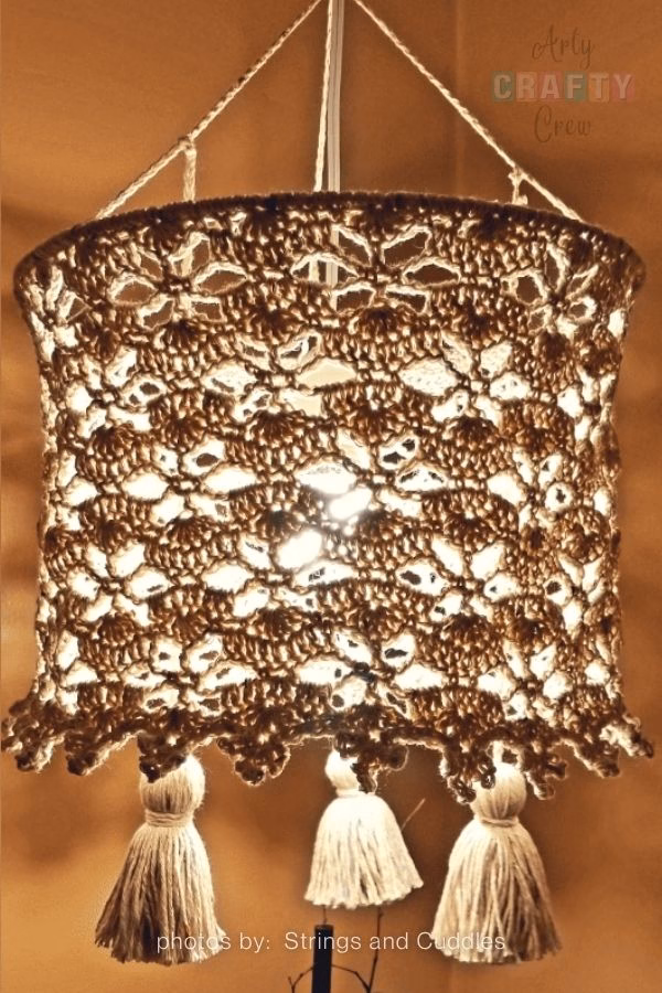 or 10. Jar Lantern Step by Step:

A detailed close-up of a glass jar lantern featuring an intricate white crochet sleeve with a delicate floral lace pattern. The jar is shown hanging from a twine handle, beautifully contrasted against a blurred background of green leaves. This image is part of a crochet roundup from https://artycraftycrew.com/.