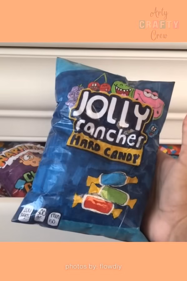A handmade paper squishy that realistically mimics a blue bag of Jolly Rancher hard candy, complete with illustrated fruit characters and candy pieces. This creative squishy idea is from https://artycraftycrew.com/.