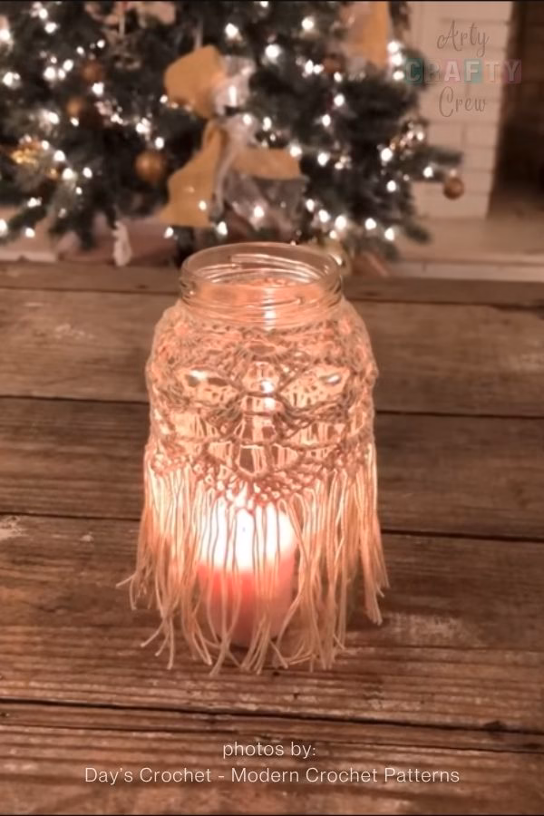 or 8. Cheap DIY Patio Lanterns:

A close-up of a glass jar repurposed into a patio lantern, featuring a vibrant orange and pink crochet sleeve with a unique open-stitch texture. The lantern is hanging outdoors from a rustic wire handle, adding a pop of color to the backyard space. This image is part of a crochet roundup from https://artycraftycrew.com/.